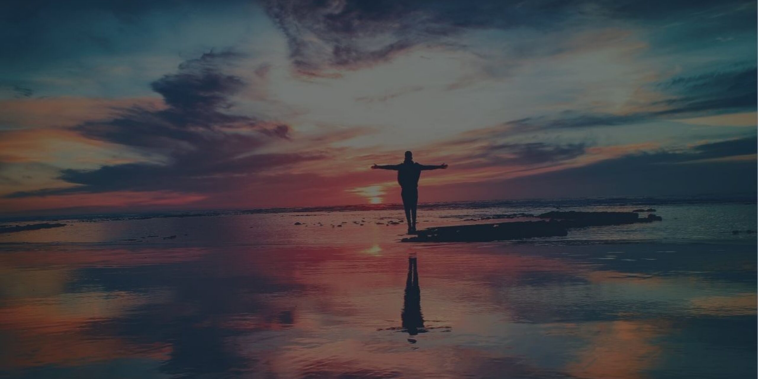 Person standing at sunset with open arms