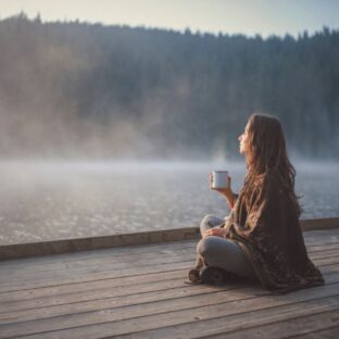 Woman sitting peacefully by lake (mindfulness)